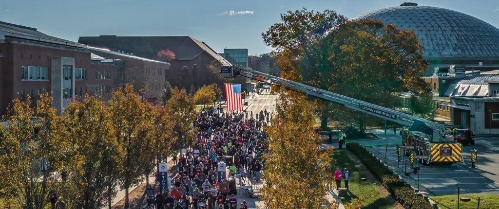 Aerial View of the 2023 Husky Run & Ruck on the UConn Campus at Storrs with a flag above the crowd at the start line.